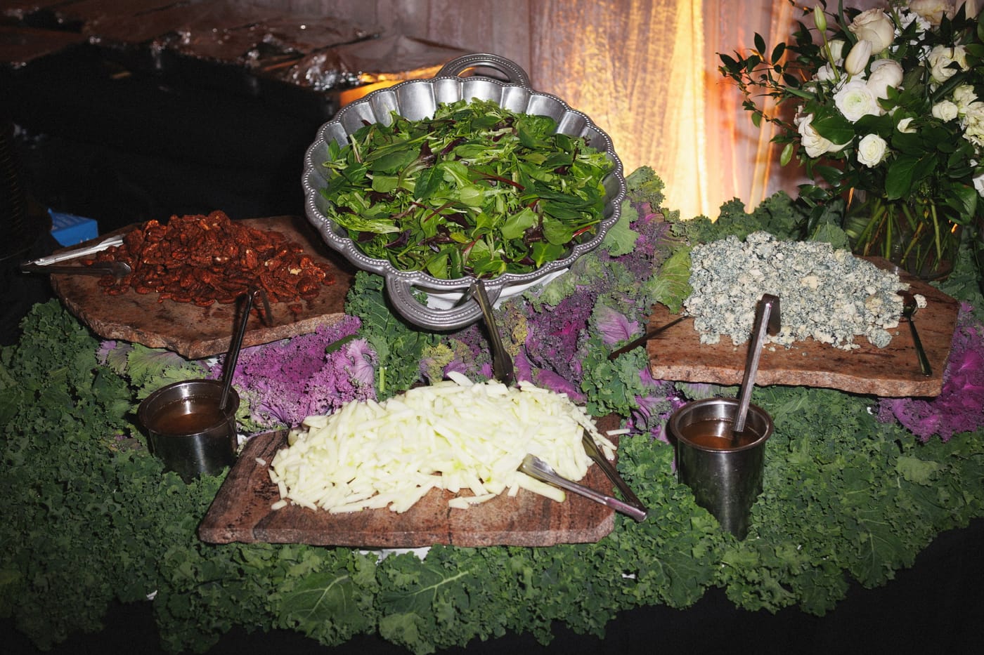 A catered salad station with pewter bowls, blue cheese and candied pecans on stone slabs