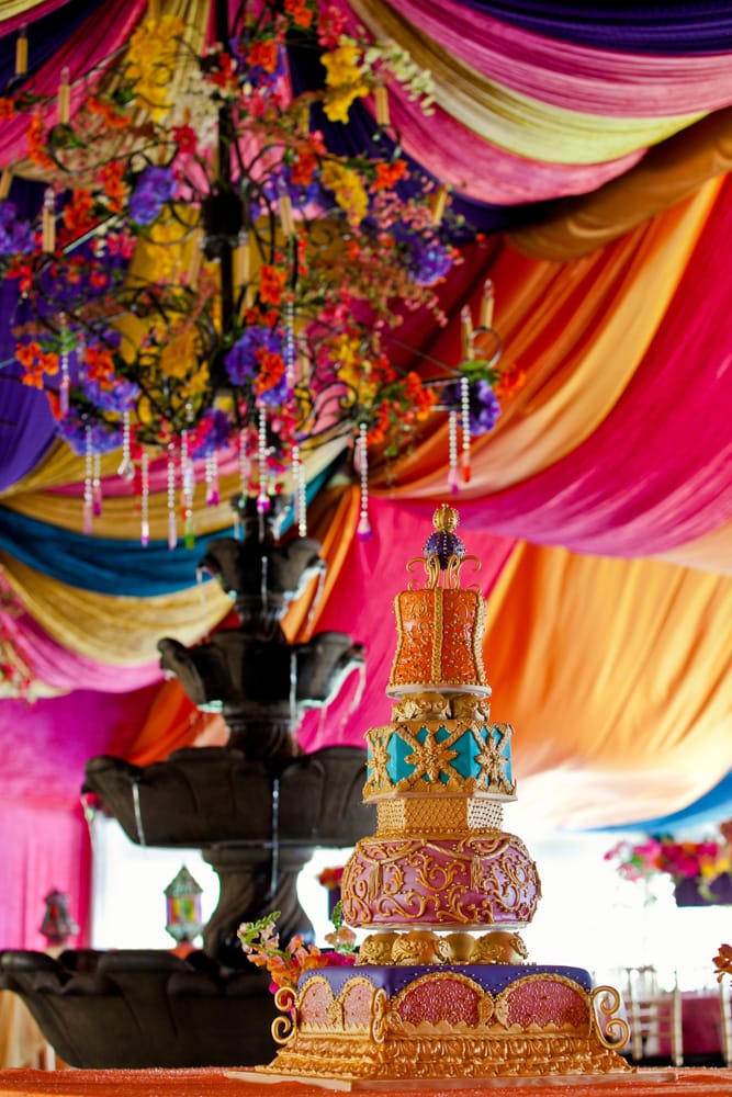 An ornate multi-tier wedding cake beneath a draped and flowered canopy